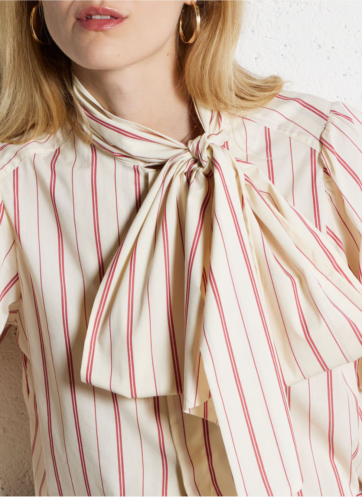 Close-up of a person wearing a cream and red striped blouse with a bow detail.