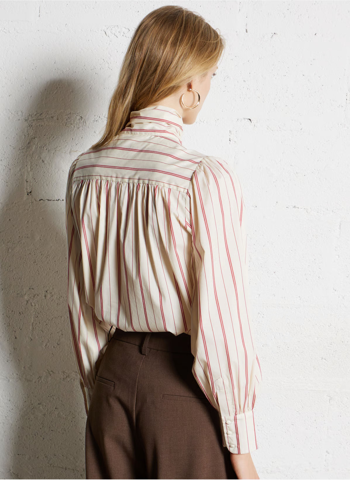 Person wearing a striped shirt and brown pants against a textured white wall