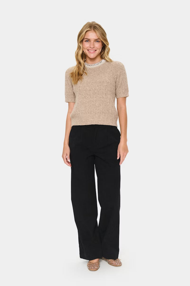 Woman wearing a beige sweater and black pants on a white background