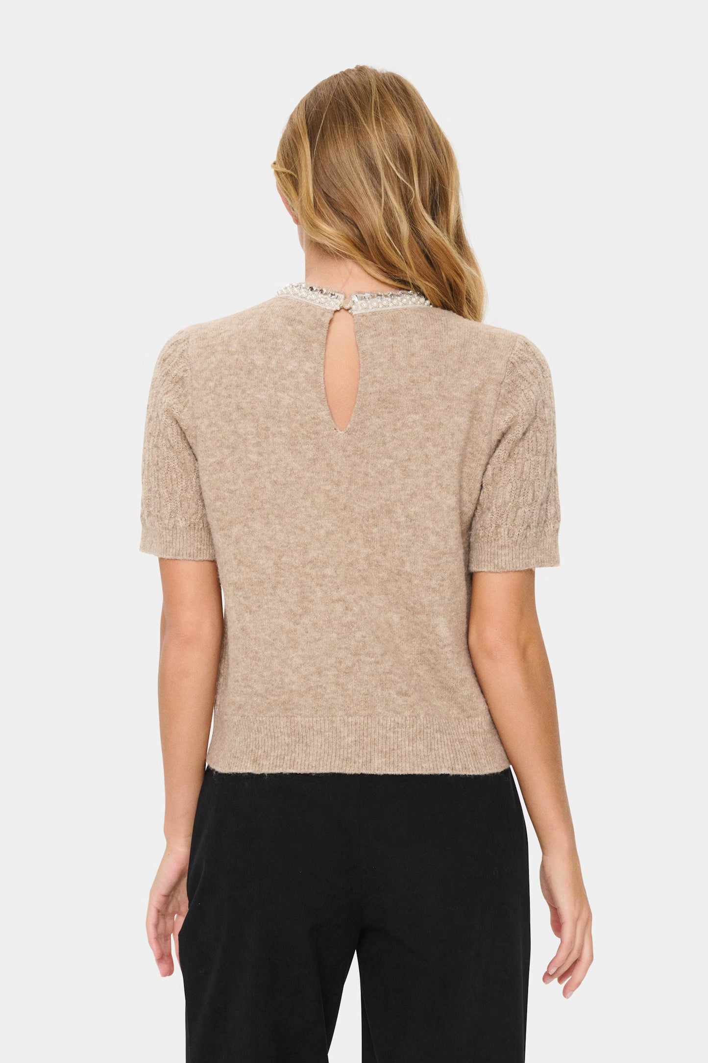 Woman wearing a beige short-sleeve top with a cut-out design on a white background
