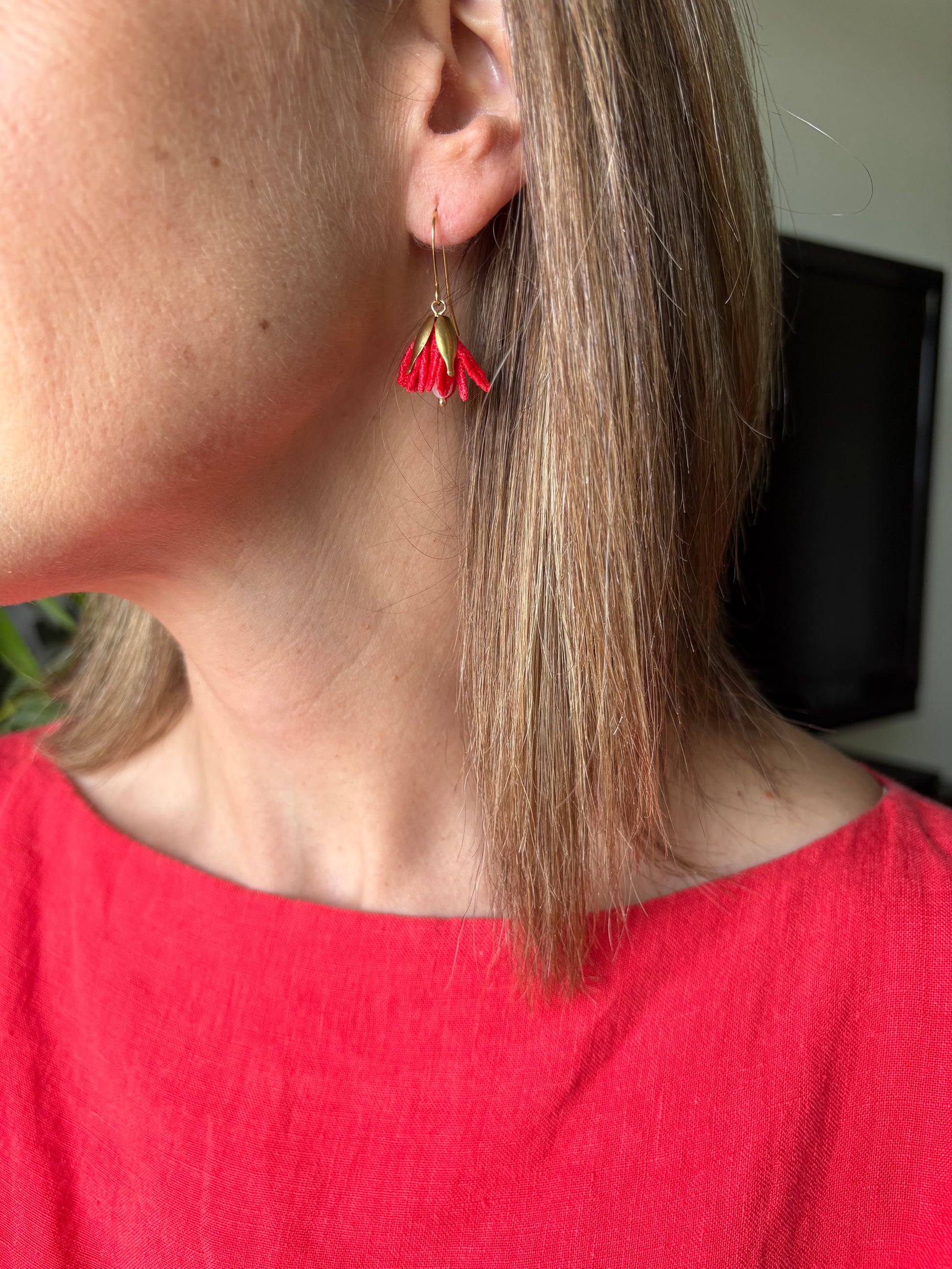 Close-up of a person wearing a red earring with a flower design.
