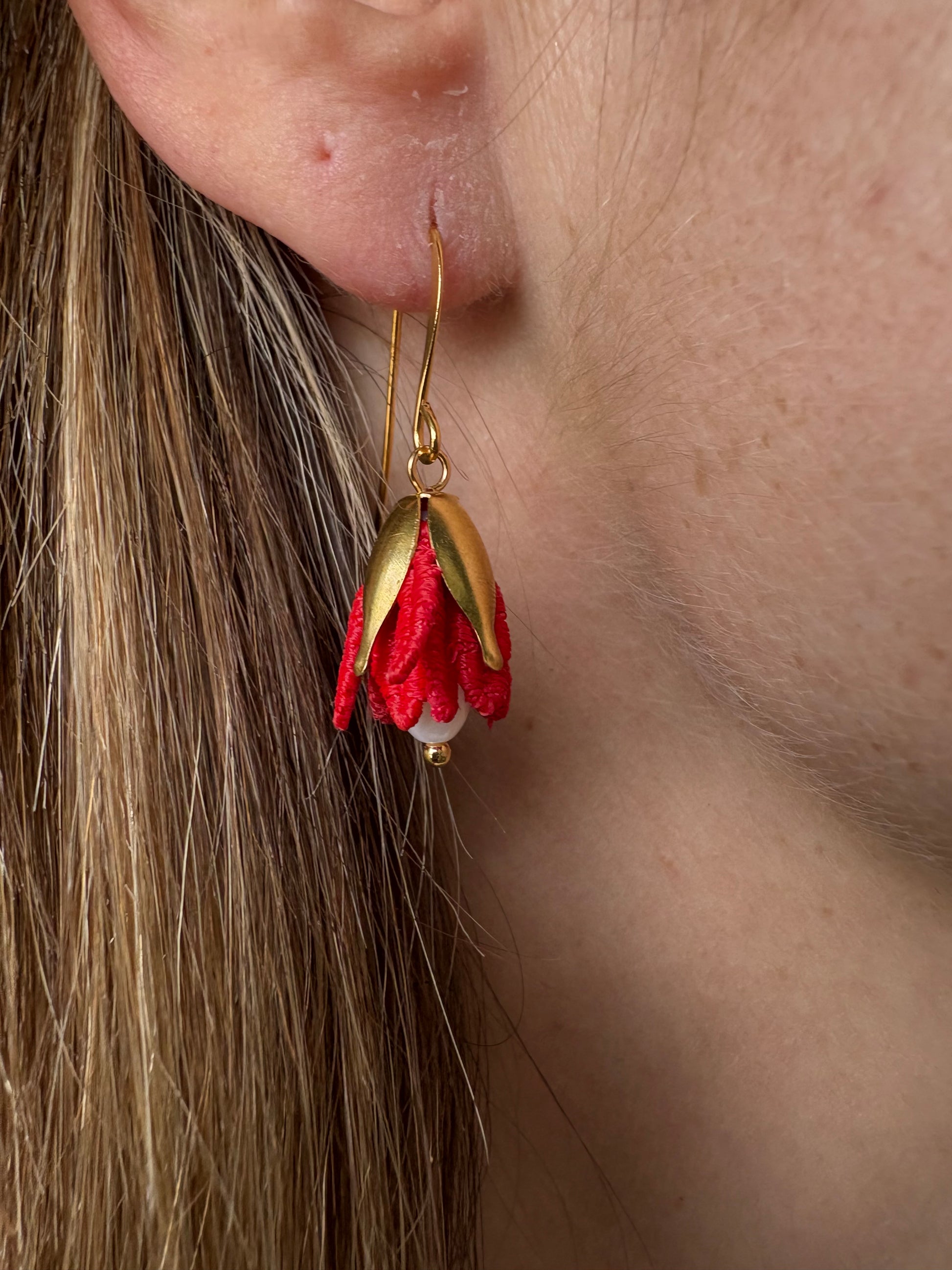 Close-up of a floral earring worn on an ear with hair in the foreground.