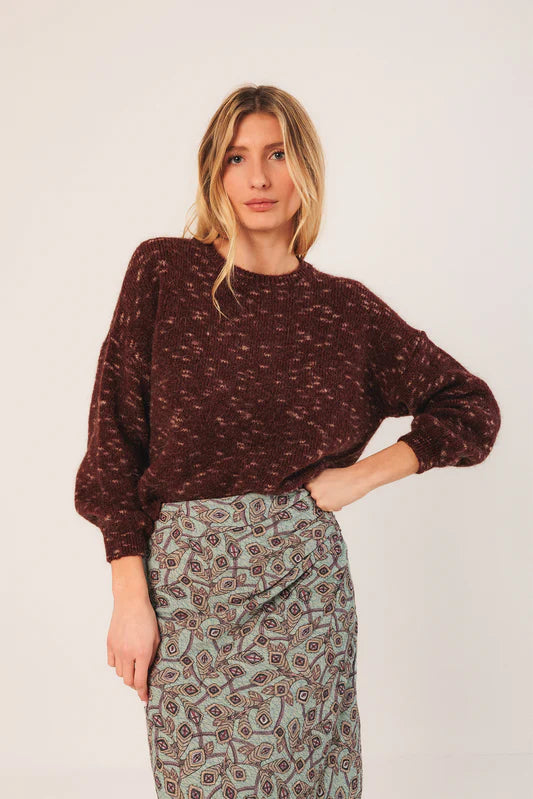 Woman wearing a patterned sweater and skirt against a plain background