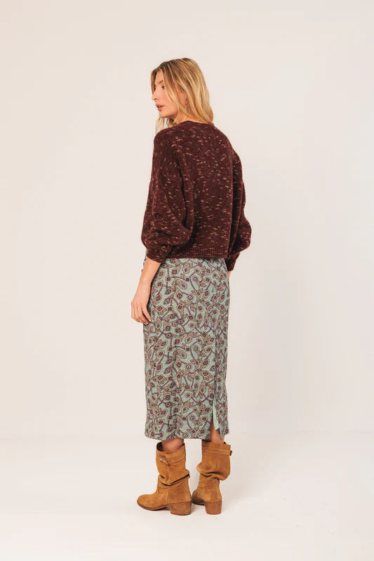 Woman wearing a brown patterned sweater and green skirt with brown boots on a white background