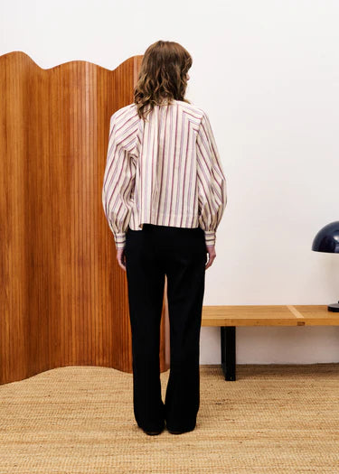 Person wearing a striped shirt and black pants standing in front of a wooden screen.