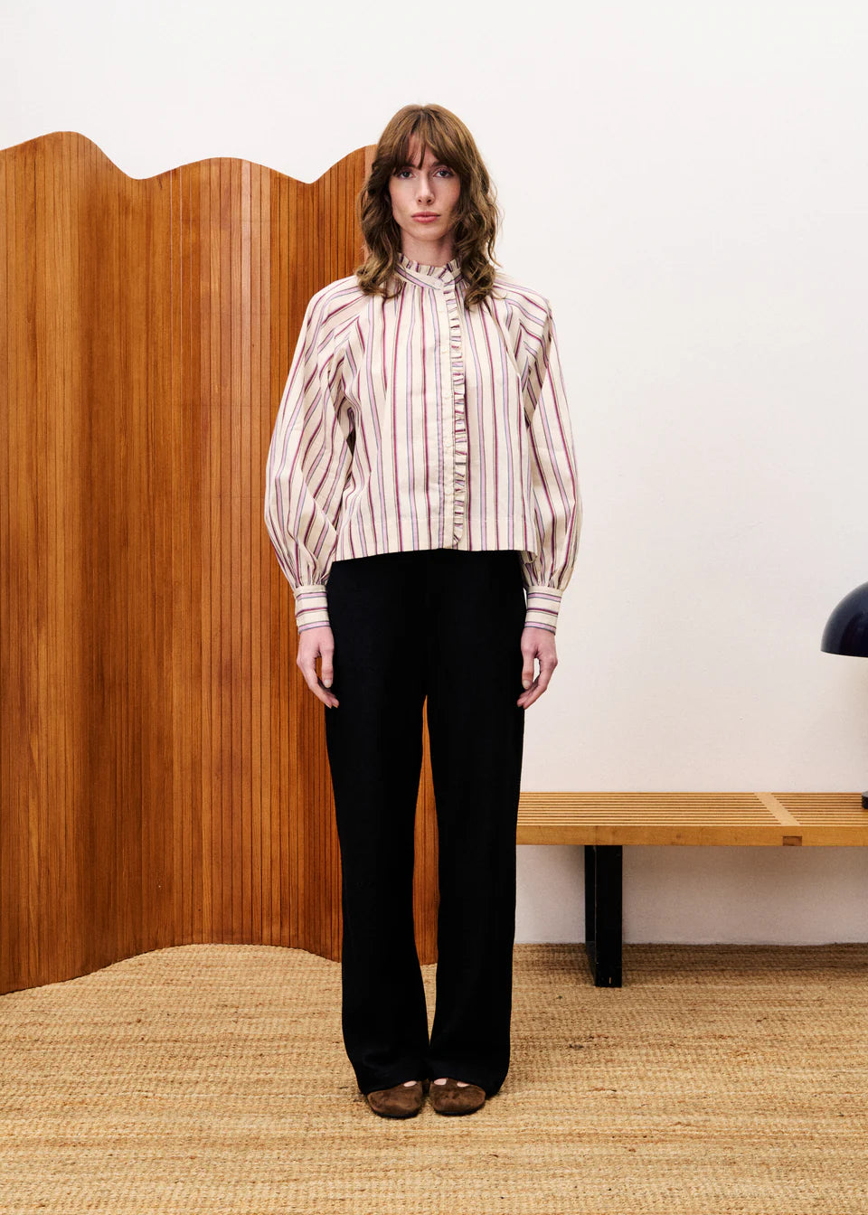 Person wearing a striped shirt and black pants standing in a room with wooden paneling.