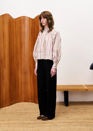 Person wearing a striped shirt and black pants standing in front of a wooden screen.