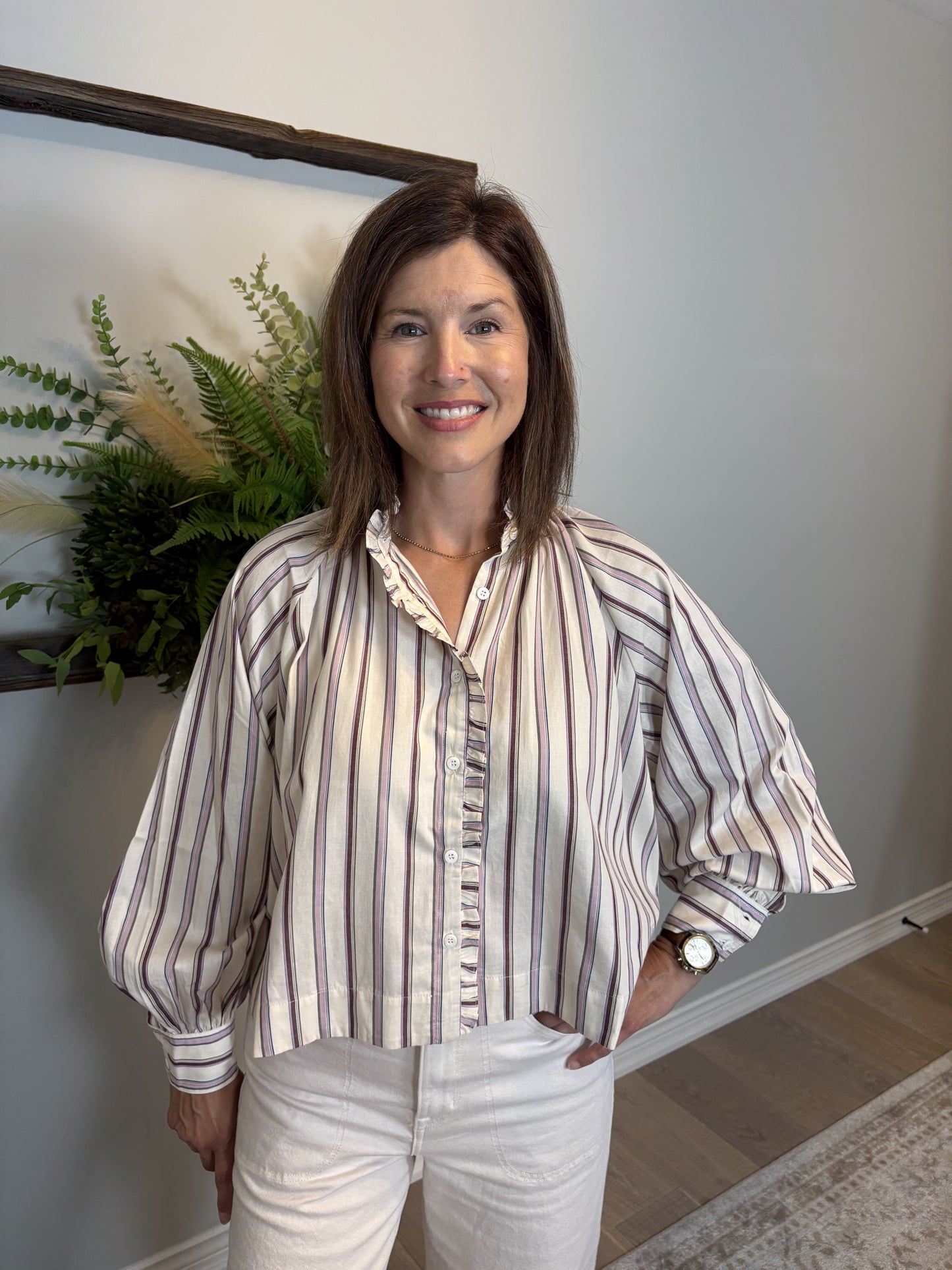 Woman wearing a striped blouse and white pants indoors with a plant in the background