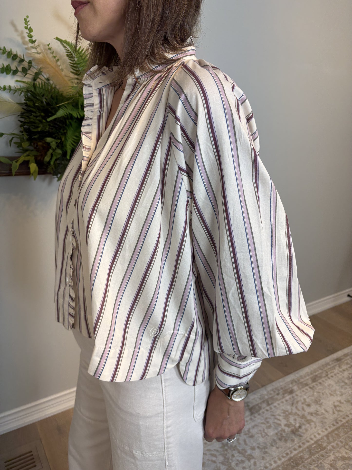 Person wearing a striped shirt in an indoor setting with a plant in the background