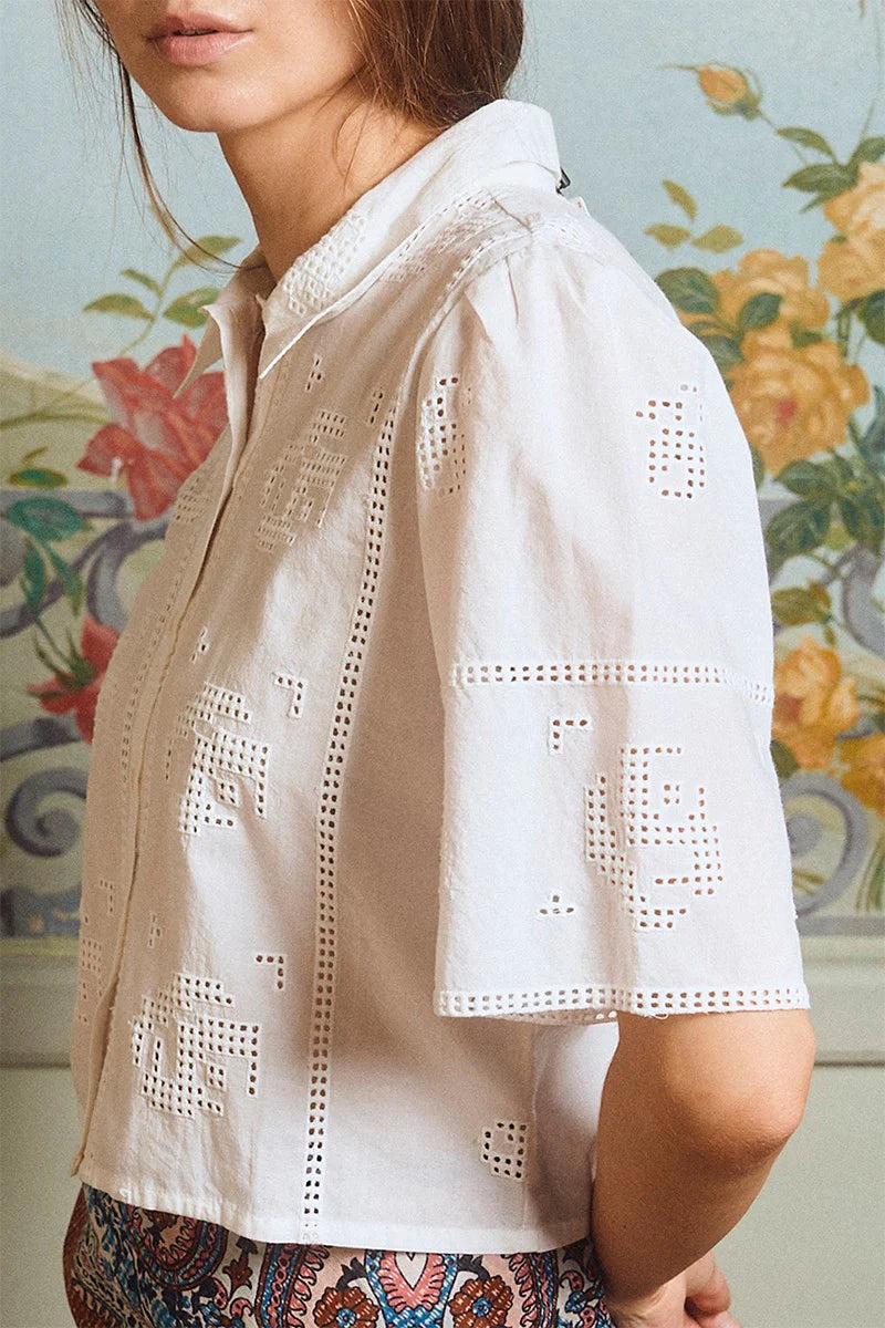 White embroidered blouse worn by a person with a floral-patterned background