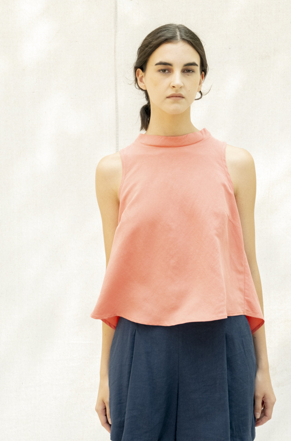 The Pacifica Top by BODYBAG by Jude features a sleeveless square design with a pleated back and a wide, layered silhouette for added movement. It sits comfortably above the waist, creating a flattering look. Made with a blend of viscose and linen, this top boasts a delicate and airy texture in a stunning salmon shade.