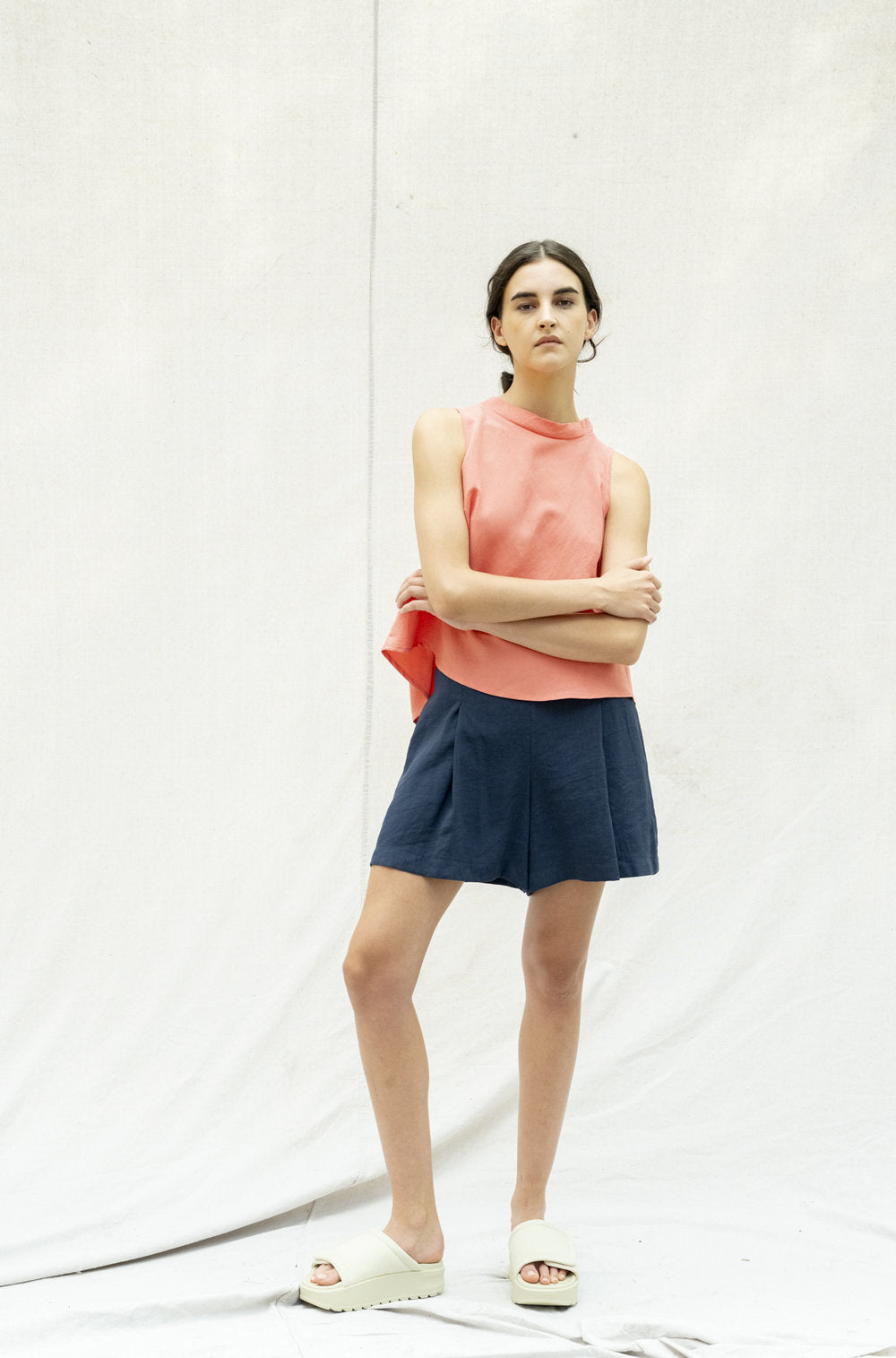 The Pacifica Top by BODYBAG by Jude features a sleeveless square design with a pleated back and a wide, layered silhouette for added movement. It sits comfortably above the waist, creating a flattering look. Made with a blend of viscose and linen, this top boasts a delicate and airy texture in a stunning salmon shade.