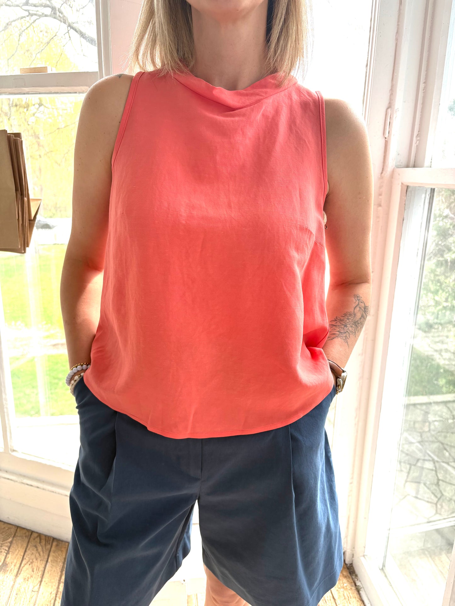 The Pacifica Top by BODYBAG by Jude features a sleeveless square design with a pleated back and a wide, layered silhouette for added movement. It sits comfortably above the waist, creating a flattering look. Made with a blend of viscose and linen, this top boasts a delicate and airy texture in a stunning salmon shade.