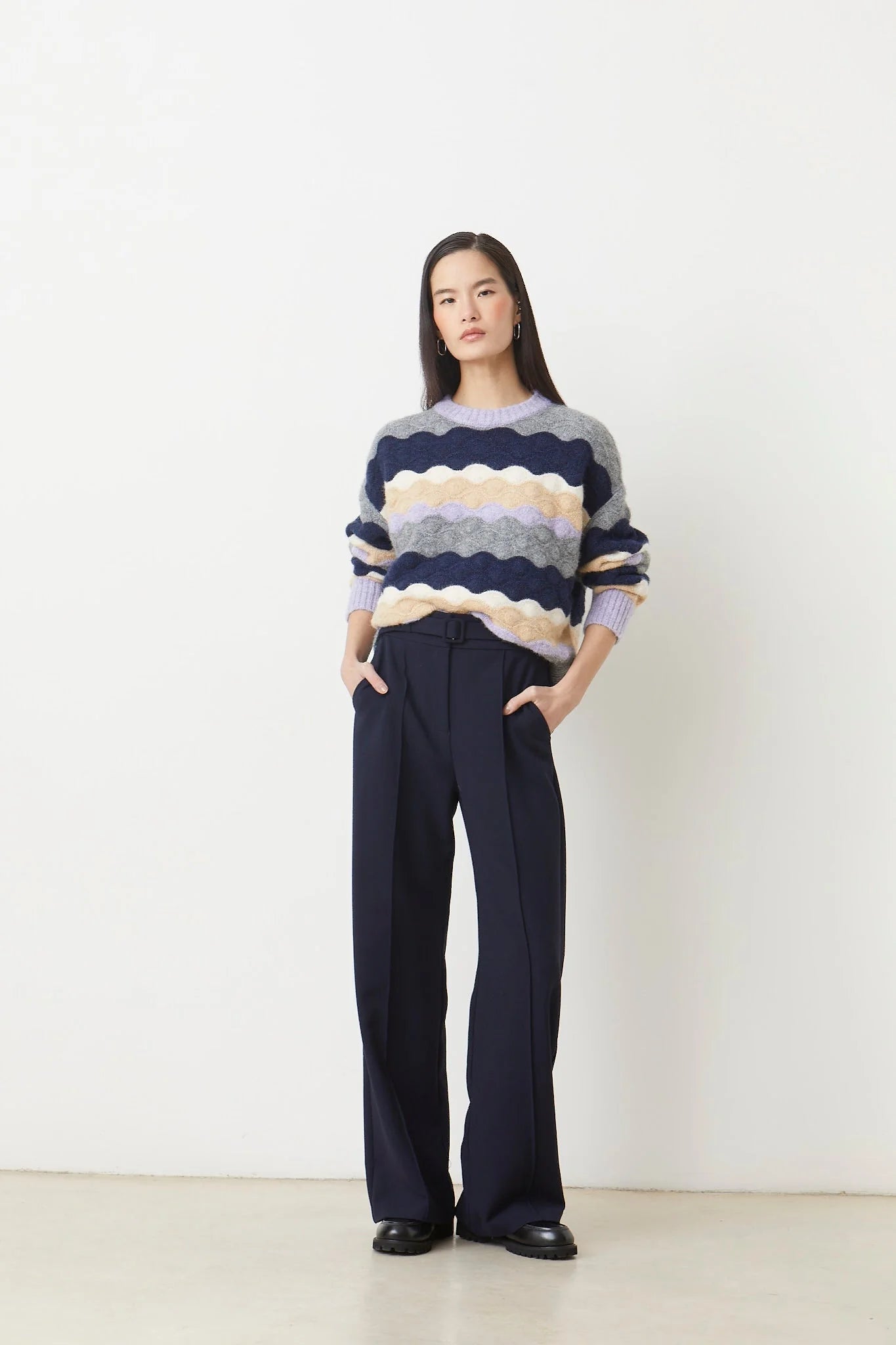 Woman wearing a striped sweater and dark pants against a white background