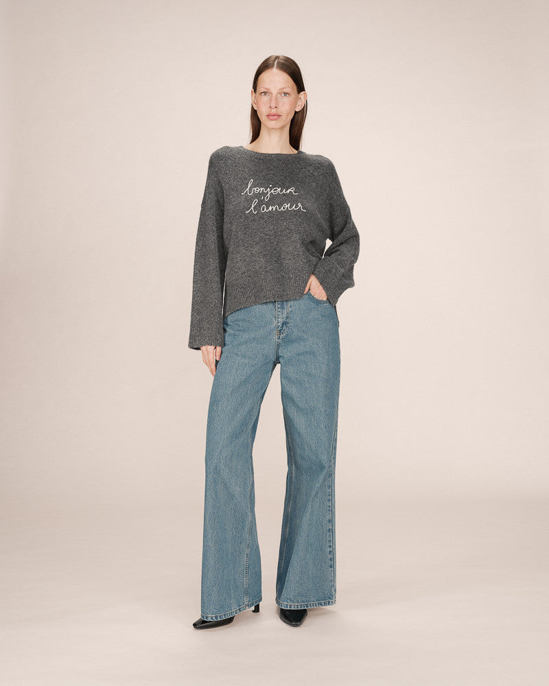 Woman wearing a gray sweater and blue jeans on a beige background