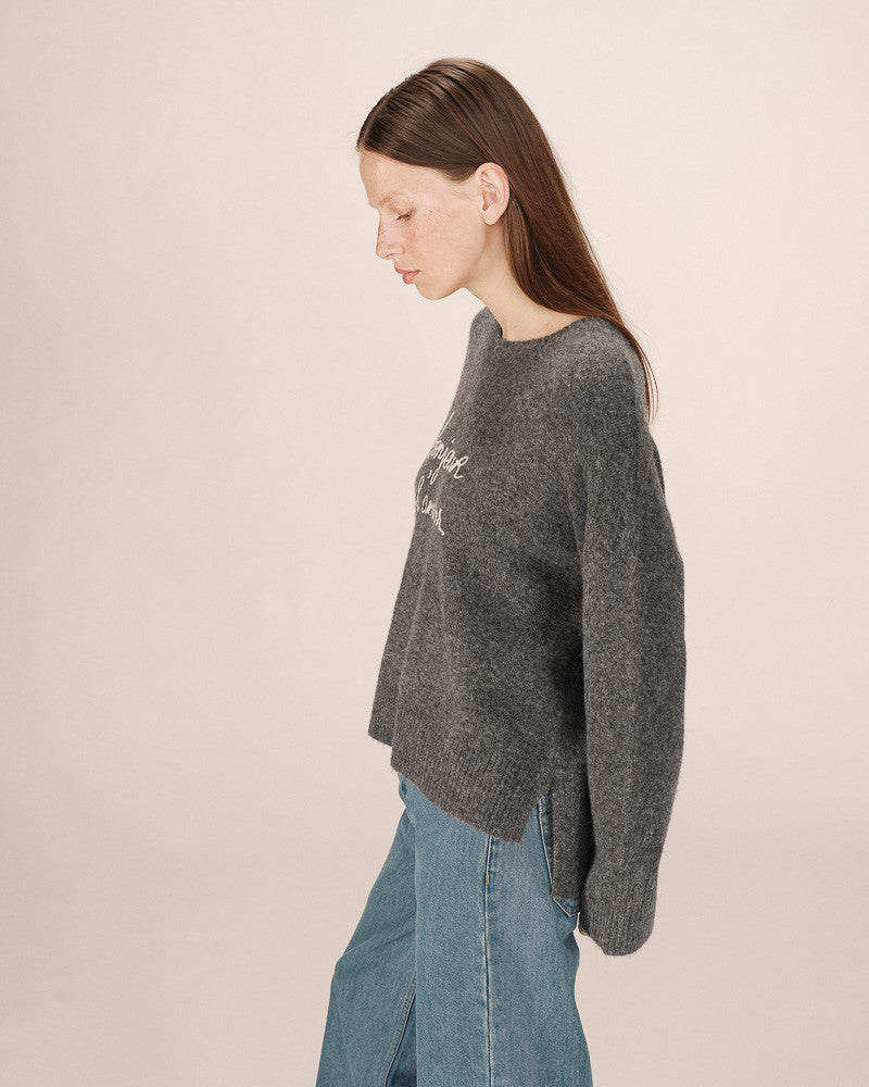 Woman wearing a dark gray sweater and blue jeans on a beige background