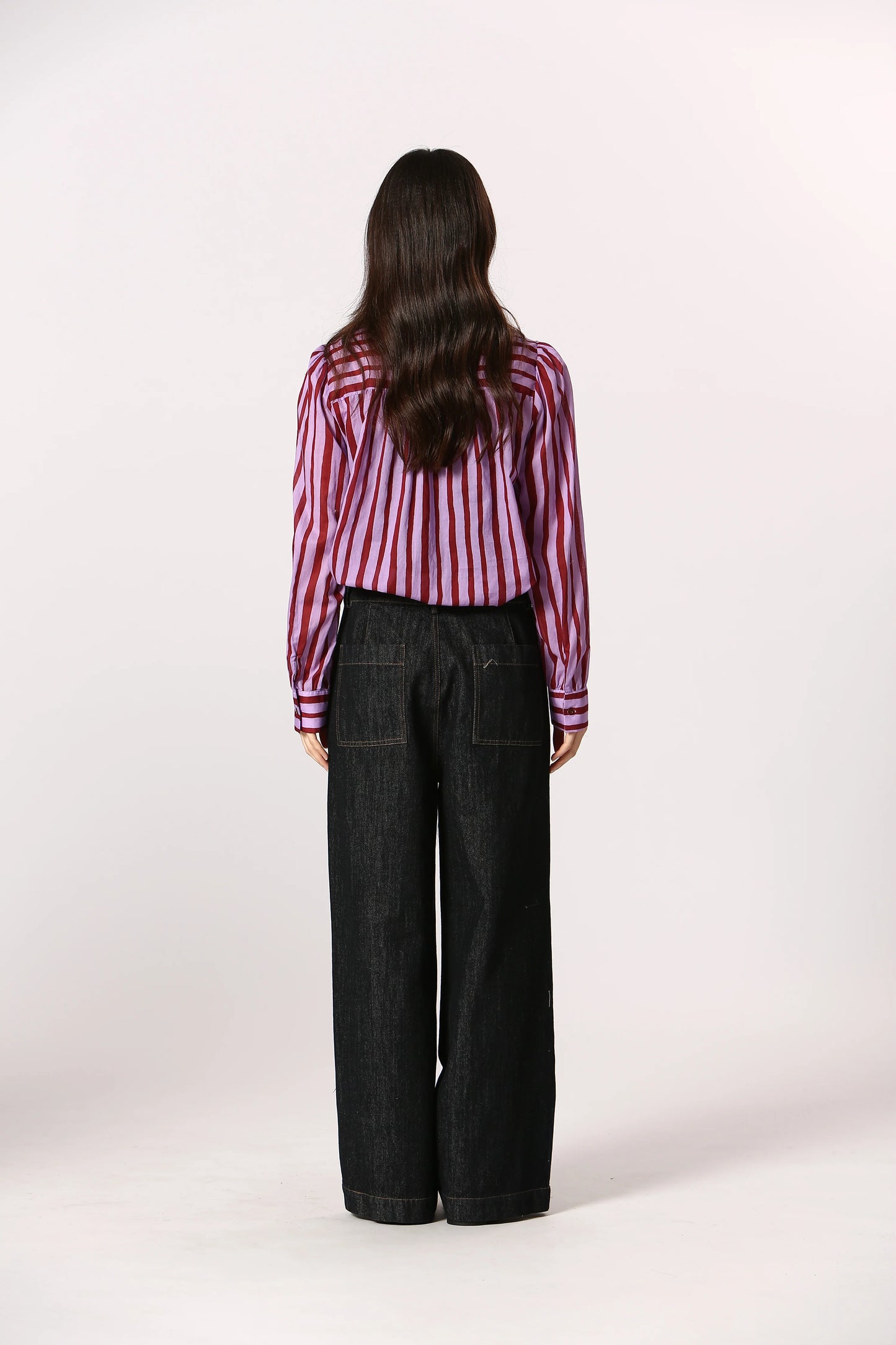 Person wearing a striped shirt and black pants on a white background
