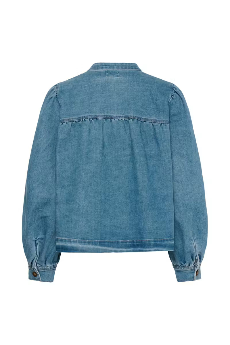 A blue denim jacket shown from the back, featuring a buttoned collar, long sleeves with buttoned cuffs, and a gathered seam across the upper back, displayed on a solid white background.