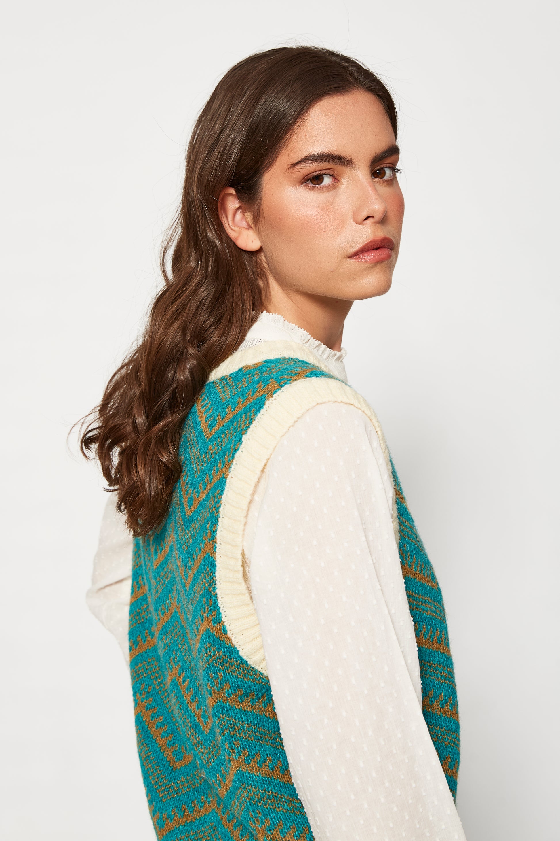 Woman wearing a patterned vest over a white shirt on a plain background