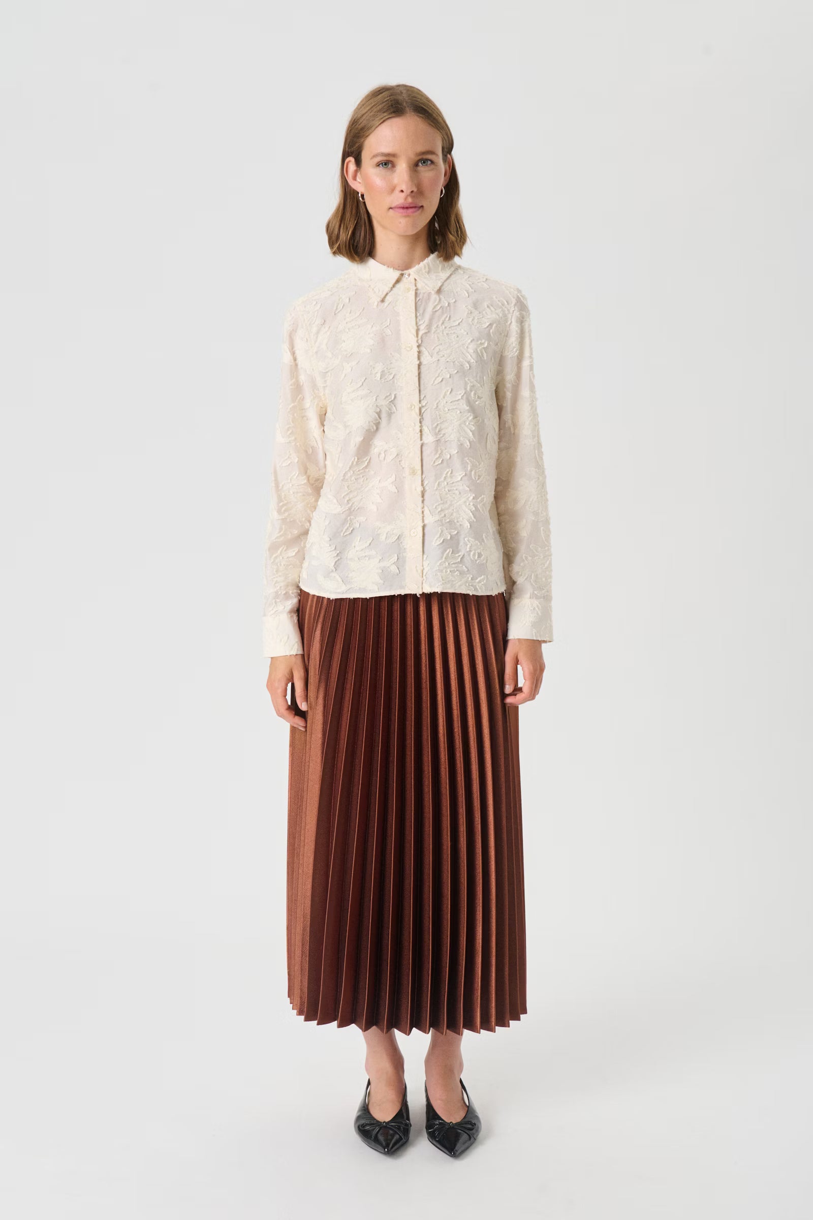 Woman wearing a white lace blouse and brown pleated skirt on a white background
