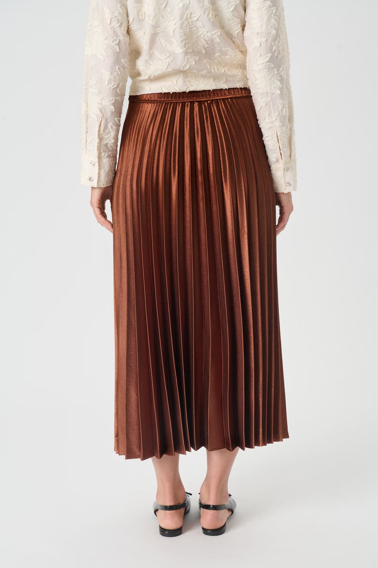 Person wearing a brown pleated skirt and white lace top on a light gray background