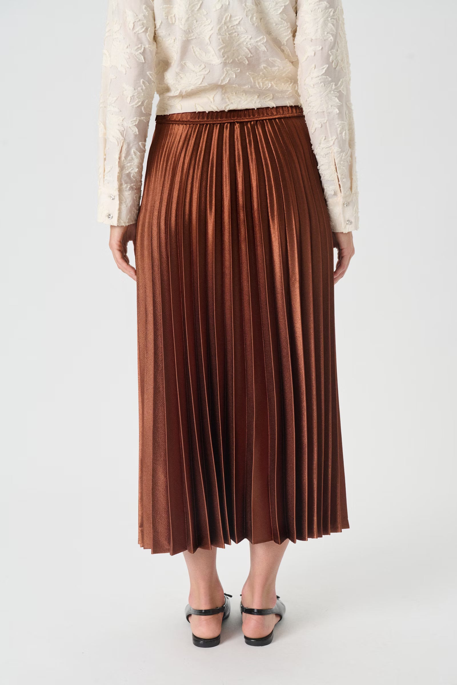Person wearing a brown pleated skirt and white lace top on a light gray background