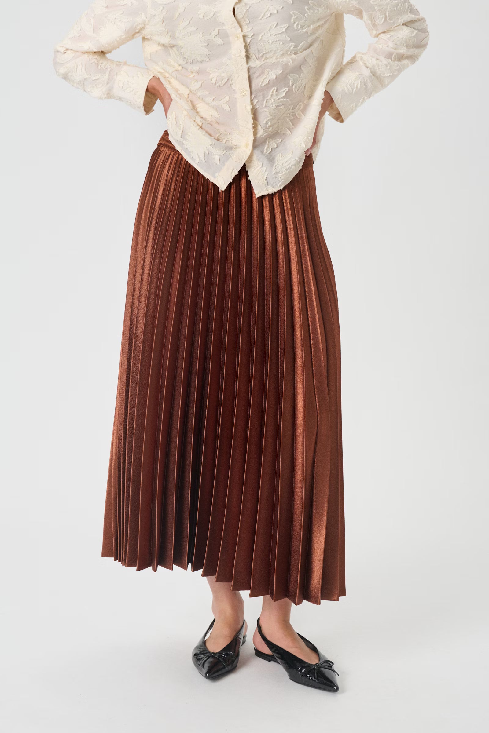 Person wearing a white blouse and brown pleated skirt on a white background