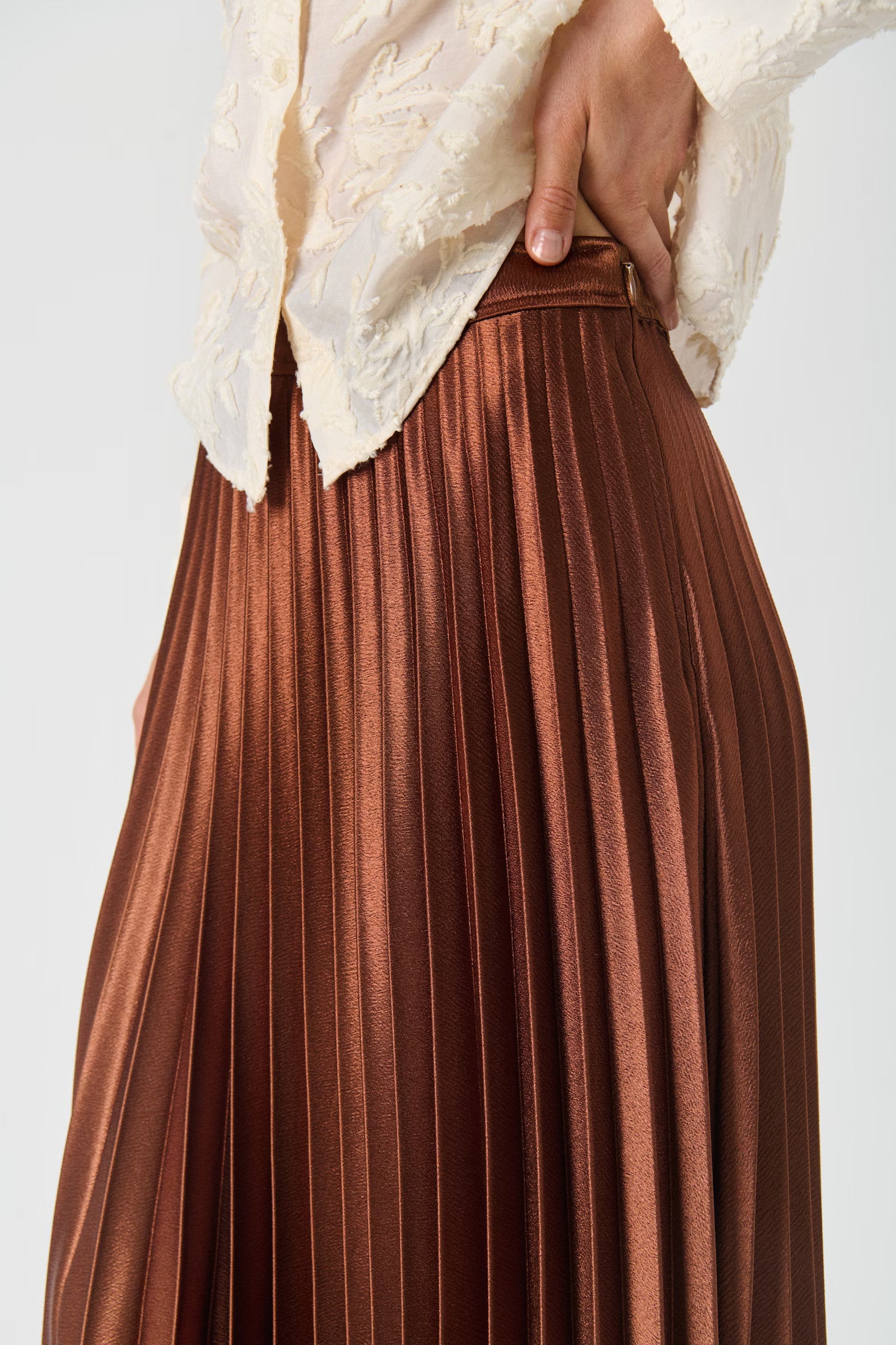Brown pleated skirt worn with a white lace top on a light gray background