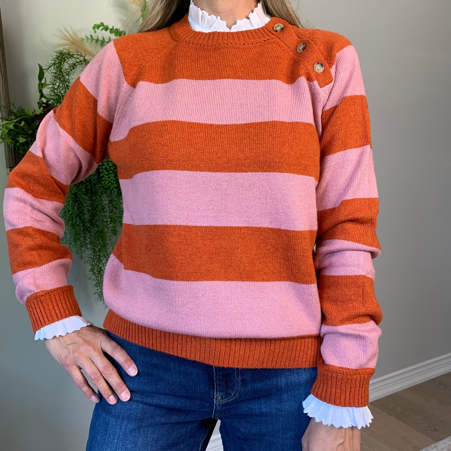 The beautiful Raya Sweater in pink and orange stripes features a round-neck with long sleeves and a 3 button detail on one shoulder.