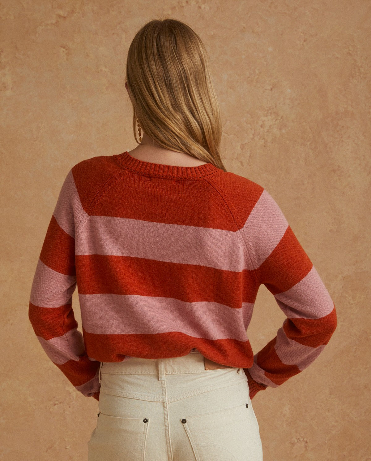 The beautiful Raya Sweater in pink and orange stripes features a round-neck with long sleeves and a 3 button detail on one shoulder.