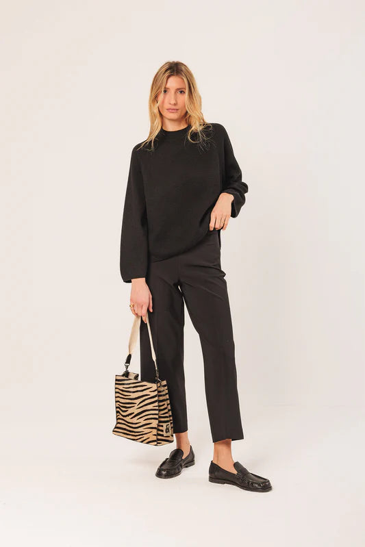 Woman wearing a black outfit holding a zebra-striped bag on a white background