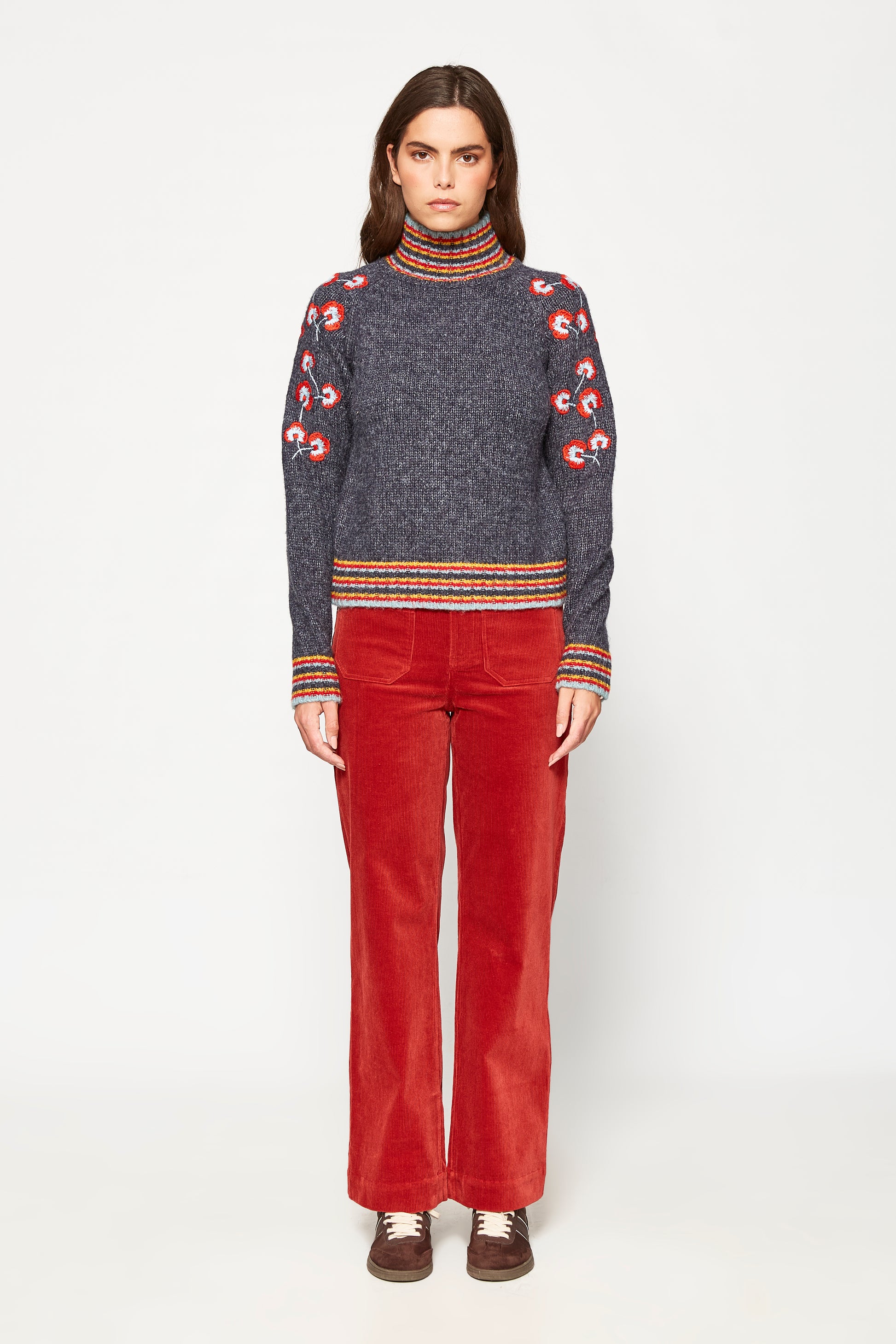 Woman wearing a patterned sweater and red pants on a white background