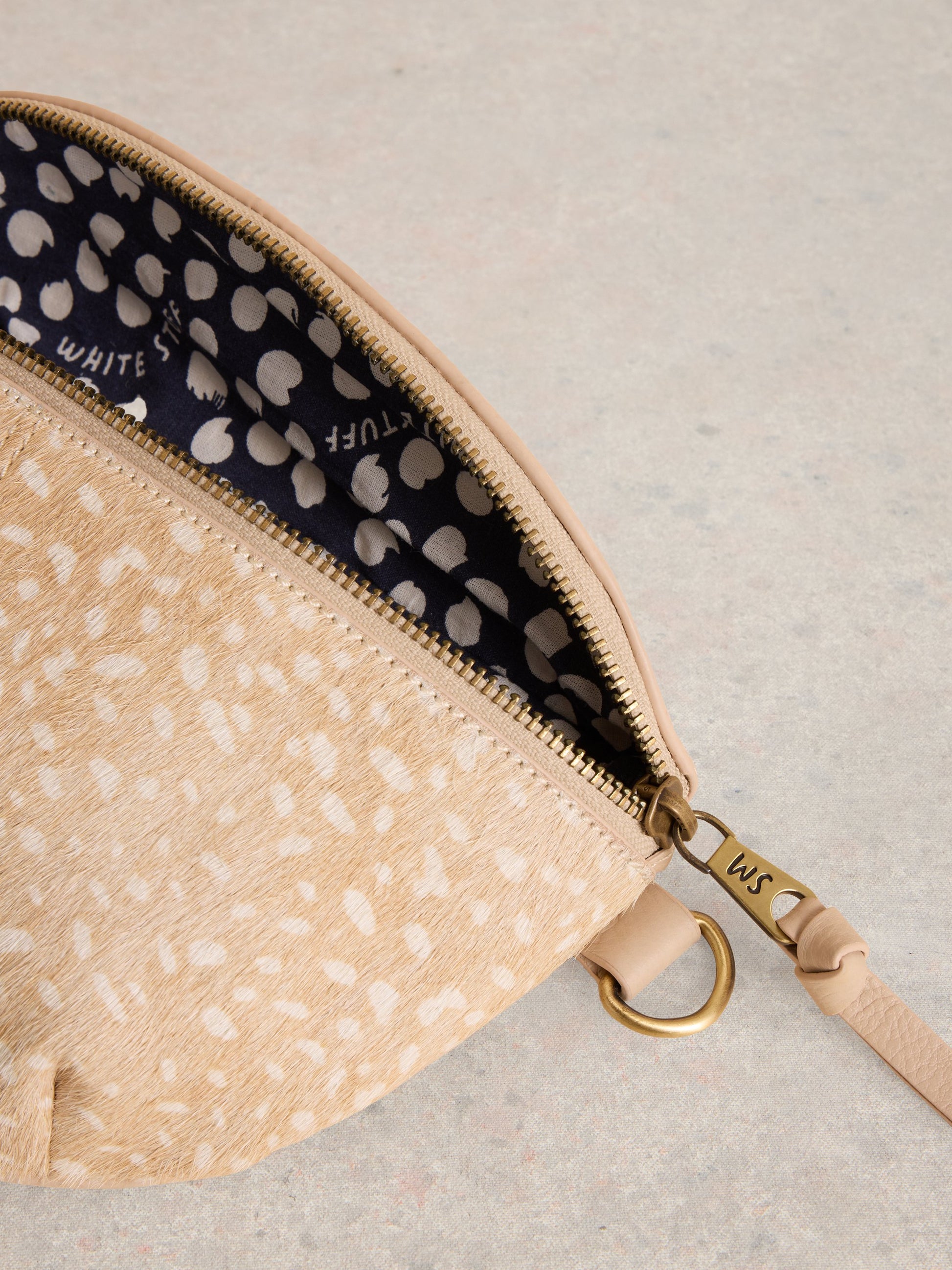 Beige patterned pouch with gold zipper and strap on a light gray background