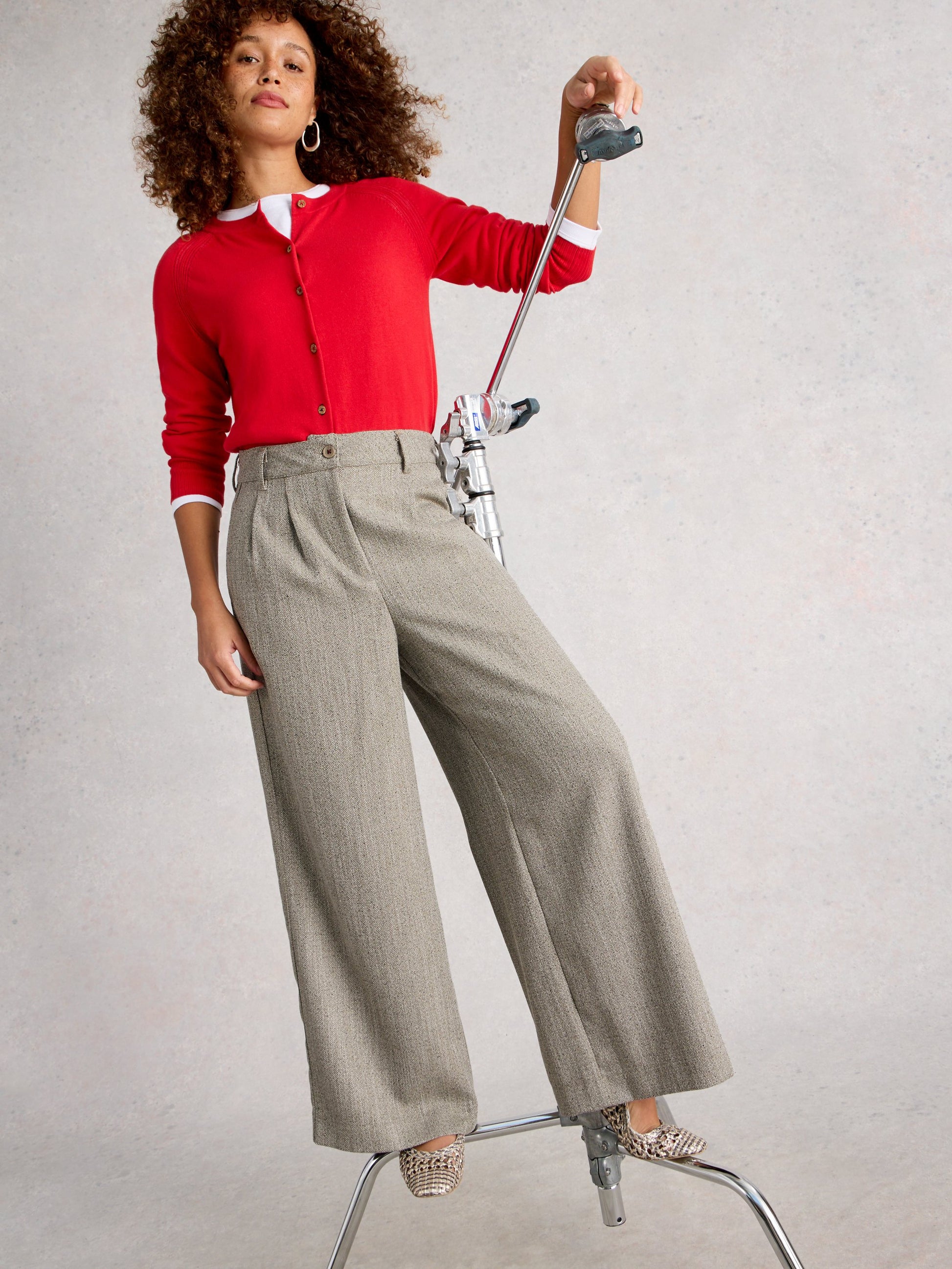 Woman in red sweater and gray pants posing with a chair on a plain background