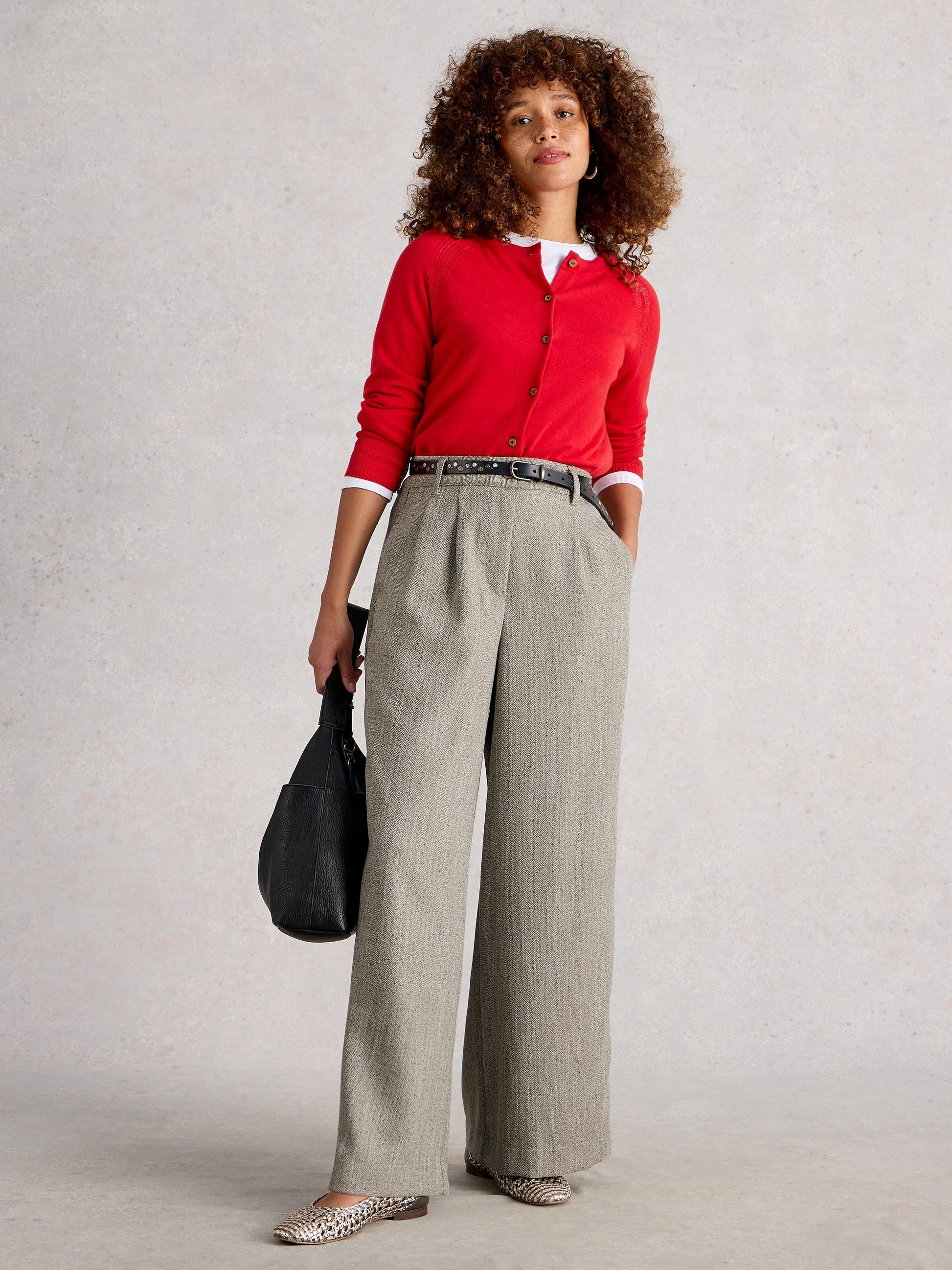Woman wearing a red cardigan and gray pants against a plain background