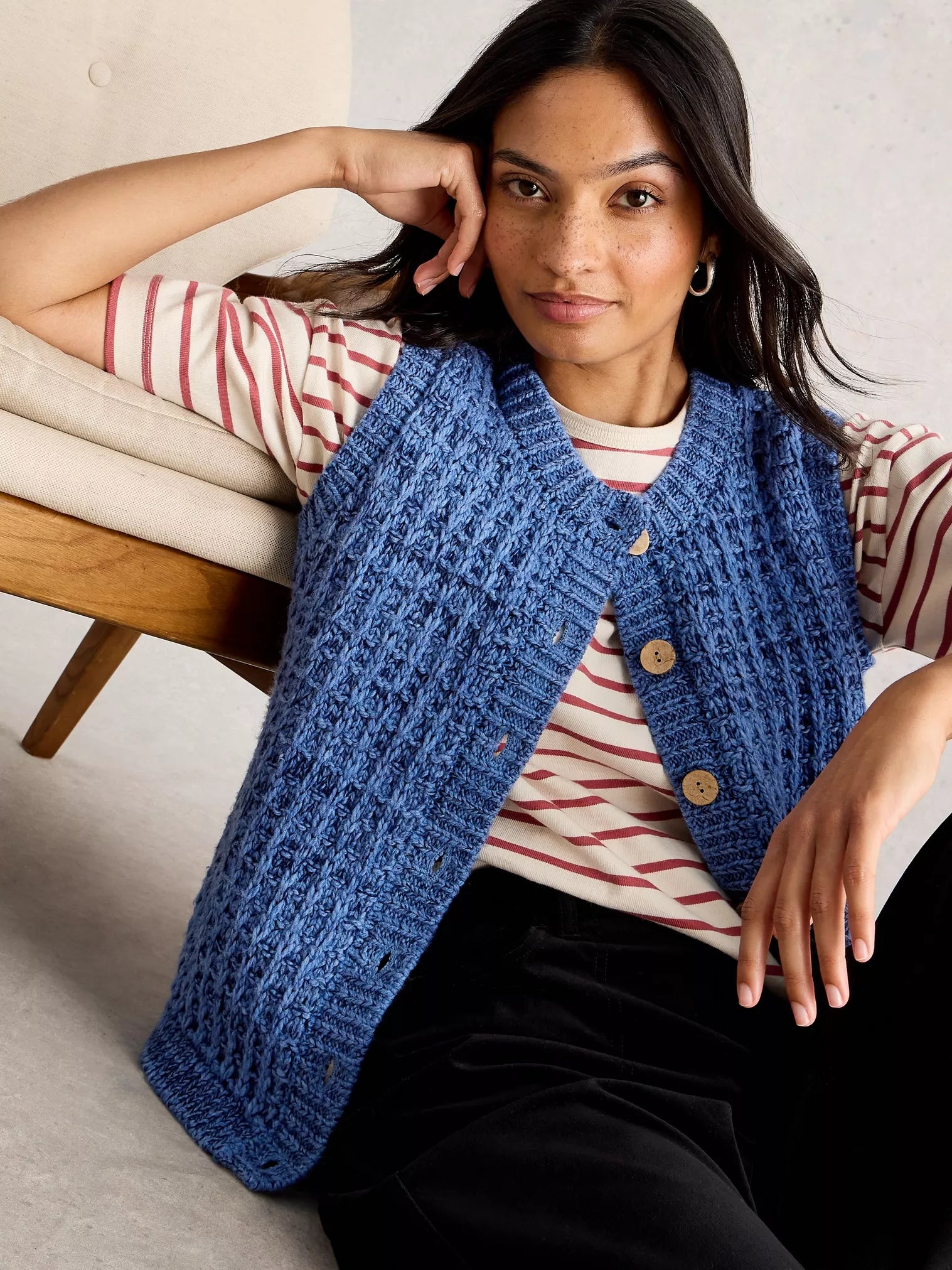 Woman wearing a blue knitted vest sitting on a couch.