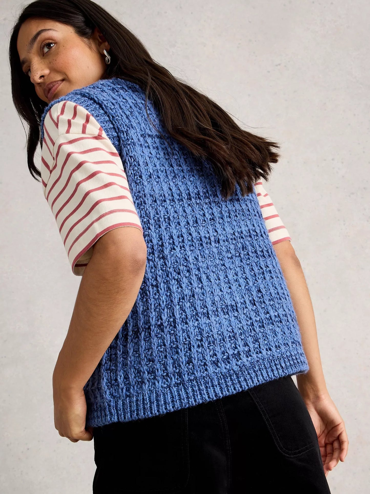 Woman wearing a blue knitted vest over a striped shirt against a plain background