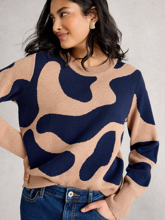 Woman wearing a beige and navy patterned sweater with blue jeans on a gray background