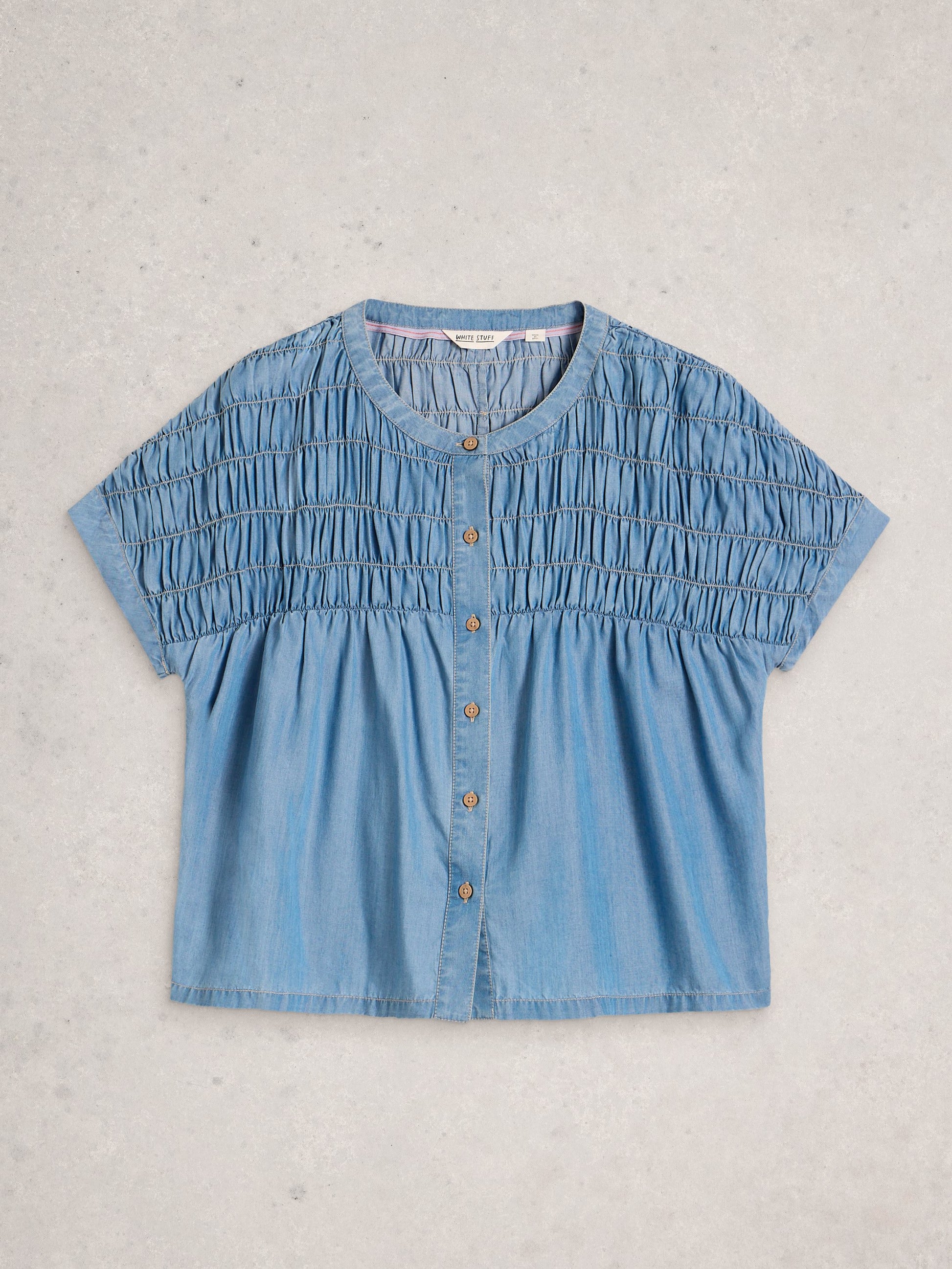 Blue denim blouse with button details on a light gray background