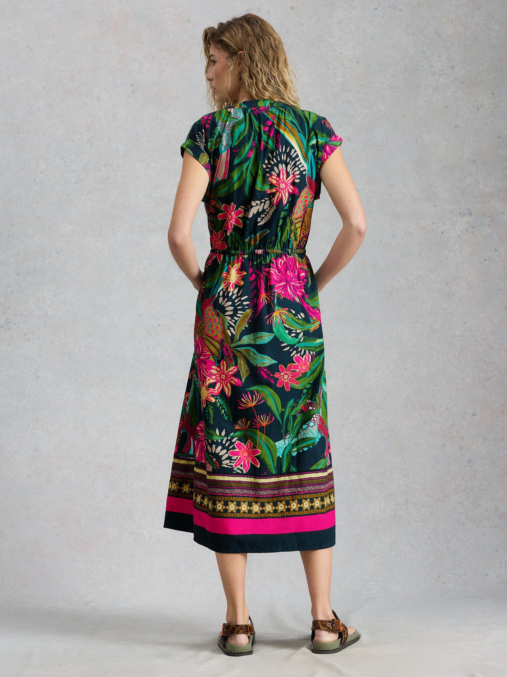 Woman wearing a colorful floral dress with a patterned hem against a plain background
