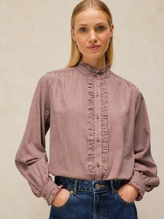 A woman wearing a long-sleeve button-front blouse with vertical stripes in dusty rose and white, paired with blue jeans, against a neutral beige background.
