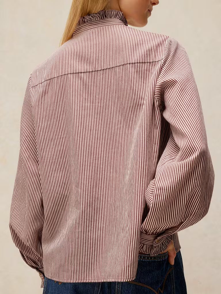 A person shown from the back wearing a long-sleeve button-up shirt with thin vertical pink and white stripes, paired with blue jeans against a plain light beige background.