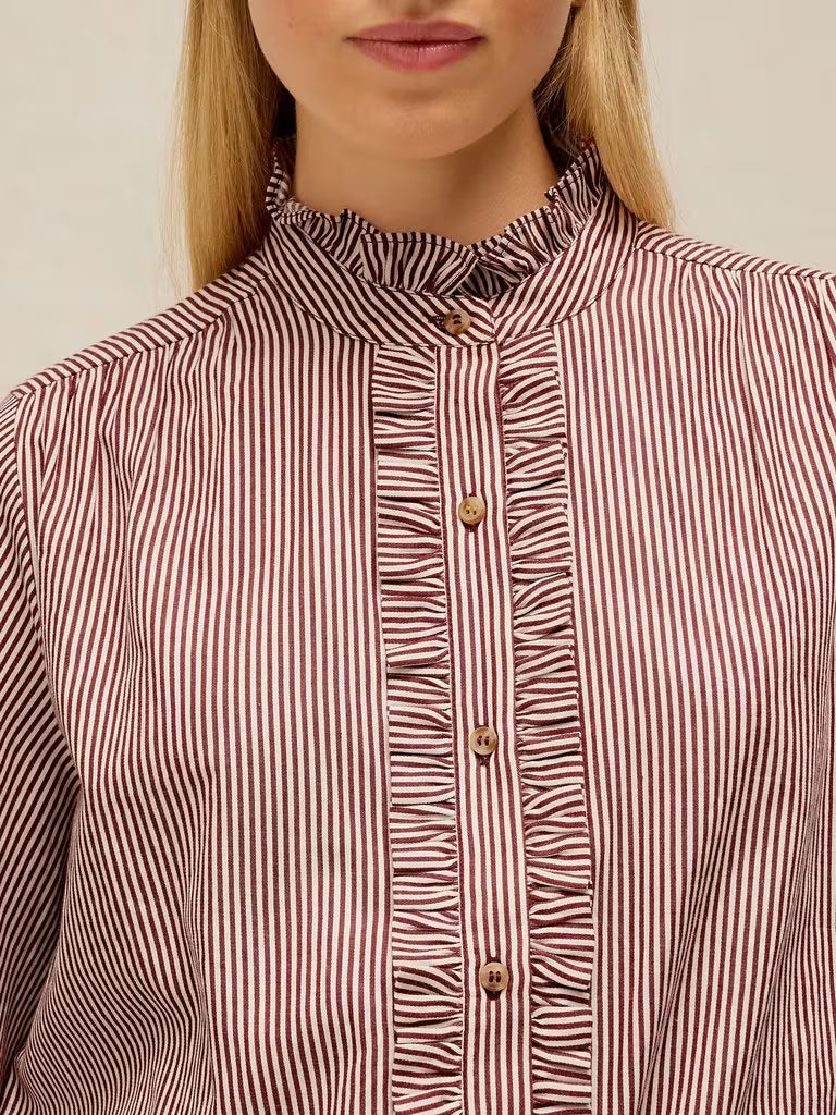 Close-up of a woman wearing a long-sleeve blouse with vertical red and white stripes, featuring a ruffled high stand collar and button-front placket with decorative gold-tone buttons.