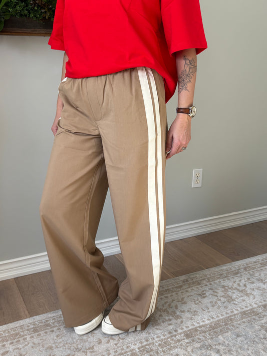 Person wearing beige track pants with white stripes in a room.