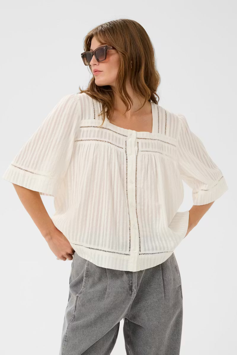 Woman wearing a white blouse with ruched details and gray pants on a white background