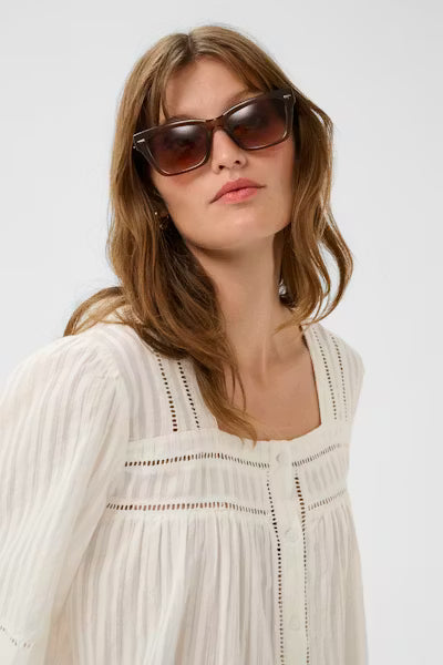 Woman wearing sunglasses and a white dress against a plain background