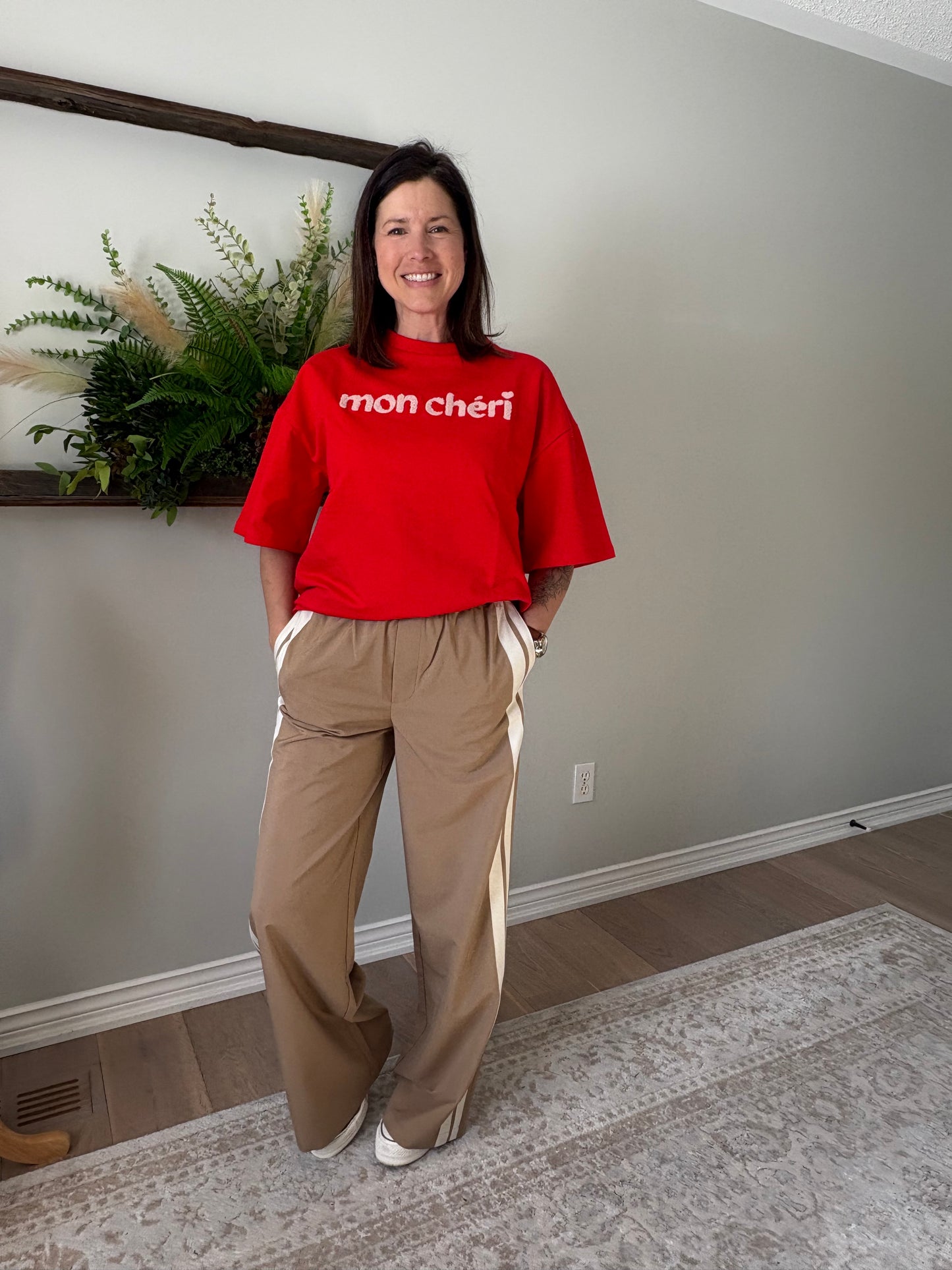 Person wearing a red hoodie with text and beige pants standing indoors.