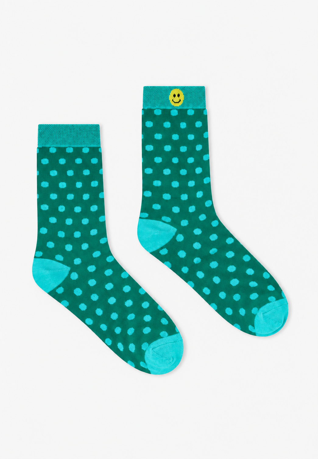 A pair of teal green socks with light blue polka dots, featuring a small yellow smiley face button on the cuff, displayed on a clean white background.