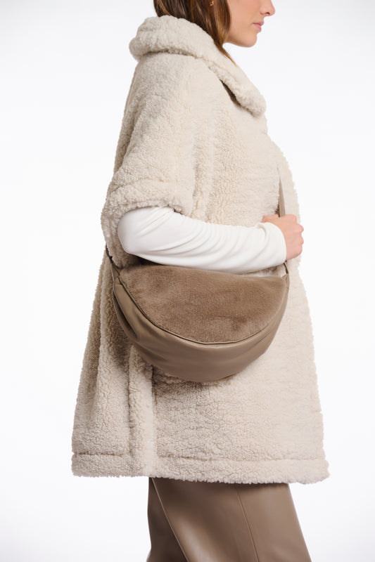 Person wearing a beige fleece-lined coat with a brown leather bag on a white background
