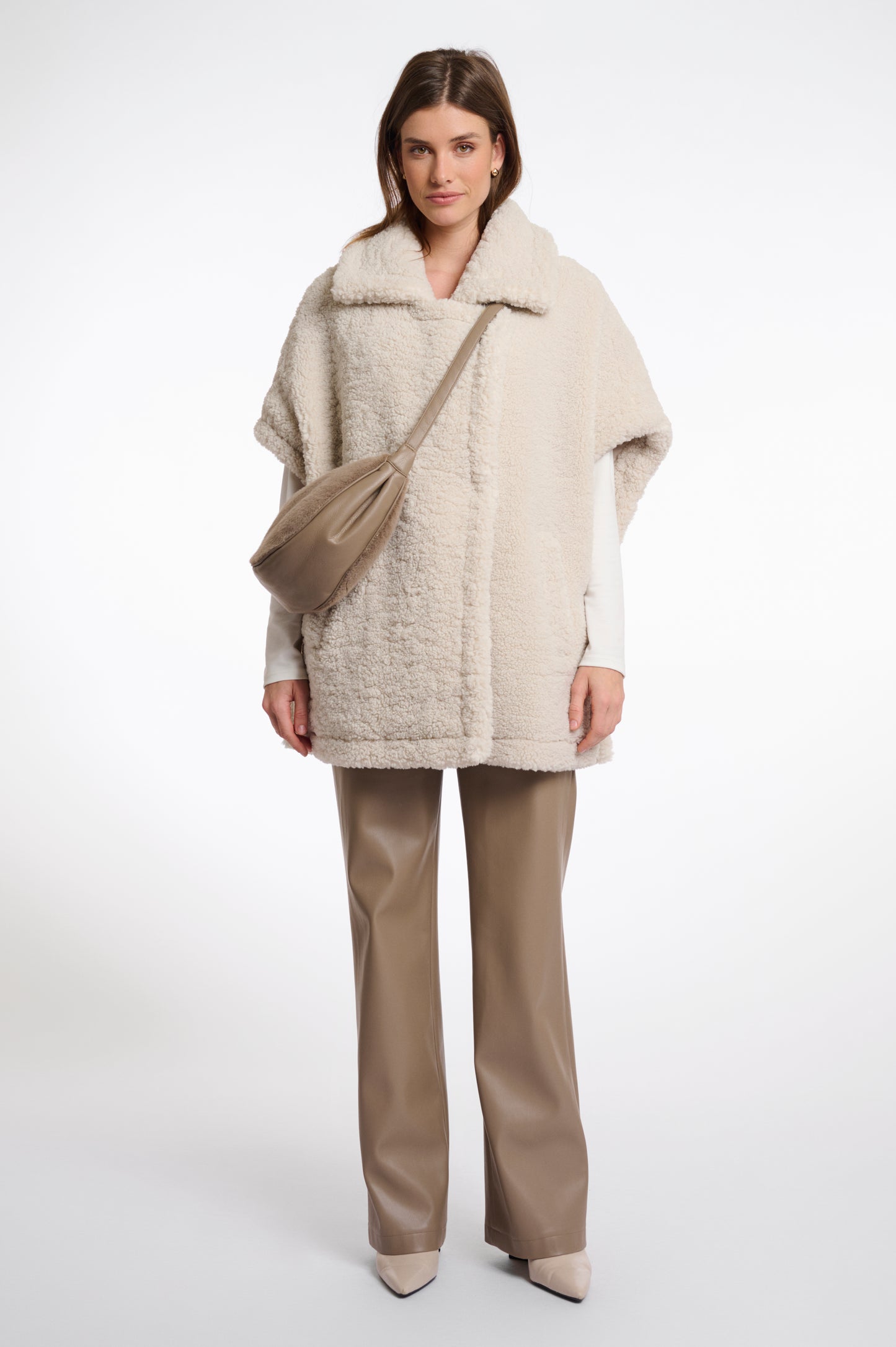 Woman wearing a beige coat and pants with a beige bag on a white background